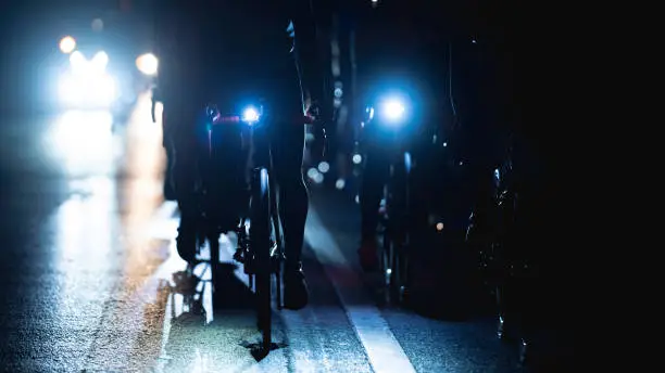 Photo of group of road bike riders at night, they turn on the headlights.noise in image.