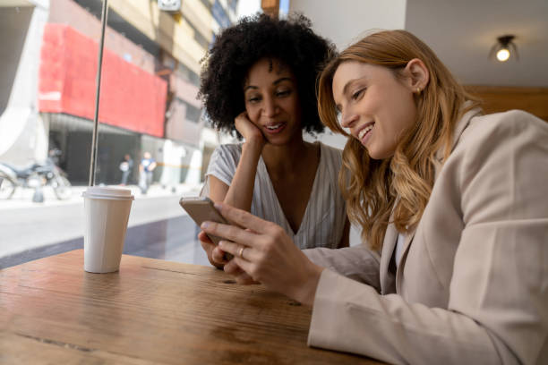istock Diverse female friends taking a break at a cafeteria dirnking a take out coffee and looking at something on smartphone 1189537897