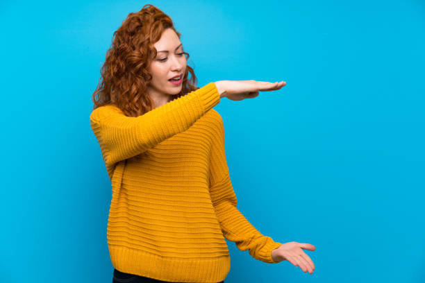istock Redhead woman with yellow sweater holding copyspace to insert an ad 1189544327