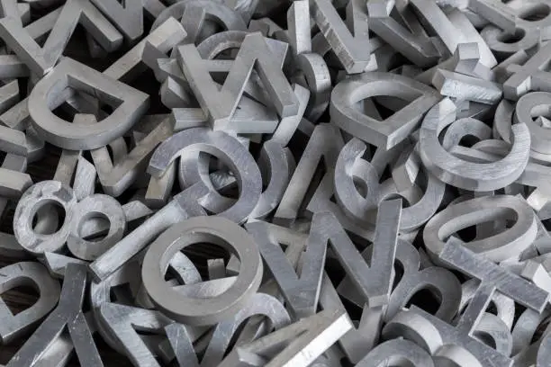 pile of silver metal alphabet characters cutted by waterjet machine - close-up view with selective focus