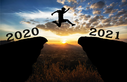 Un joven salta entre 2020 y 2021 años sobre el sol y a través de la brecha de la silueta de la colina noche cielo colorido. photo