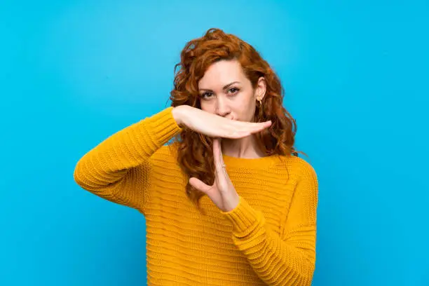 Redhead woman with yellow sweater making time out gesture