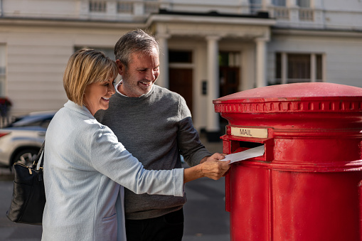 Happy adult couple putting a letter in the mail and smiling â lifestyle concepts