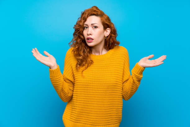 istock Redhead woman with yellow sweater having doubts while raising hands 1189549368