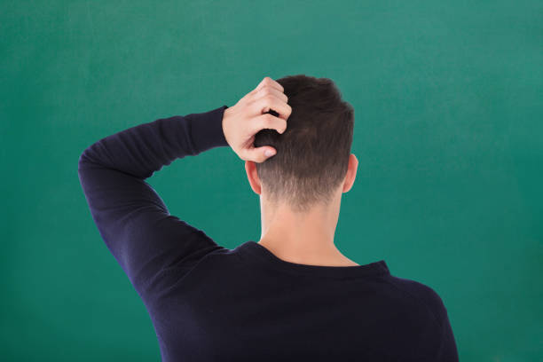 Rear View Of Young Man In Blue T-shirt Scratching His Head Against Green Background