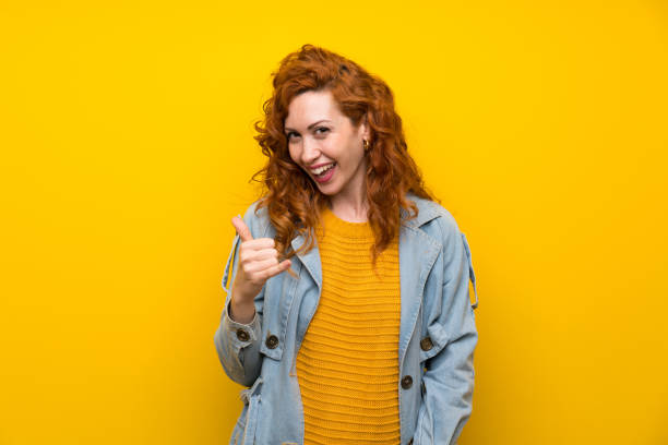 istock Redhead woman over isolated yellow background making phone gesture 1189553934