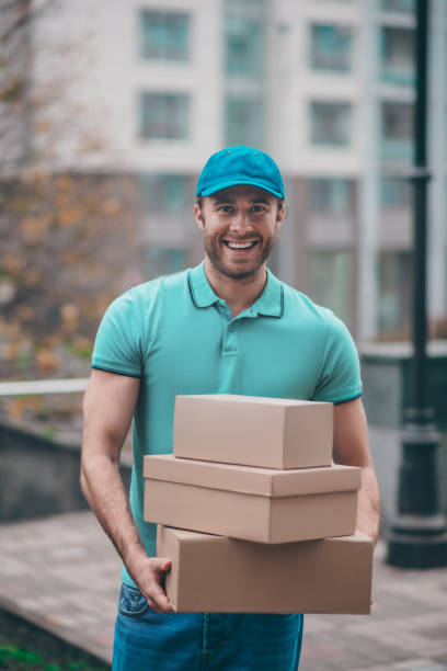 istock Smiling delivery man wearing cap holding boxes for clients 1189555110