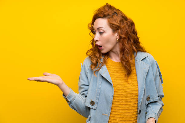 istock Redhead woman over isolated yellow background holding copyspace imaginary on the palm 1189556033