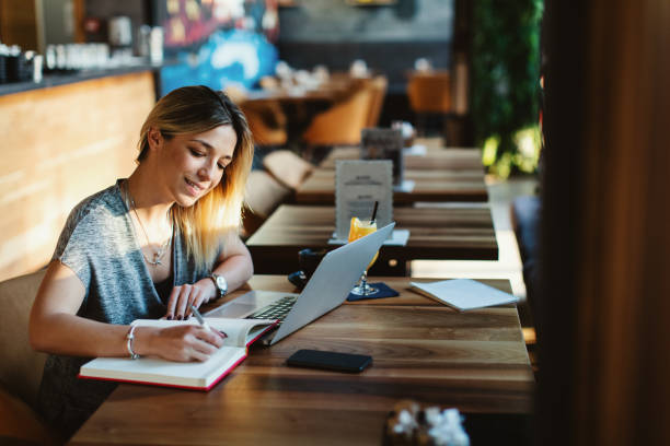 istock Young woman writing a note with pen with laptop on table at a coffee shop. 1189557828