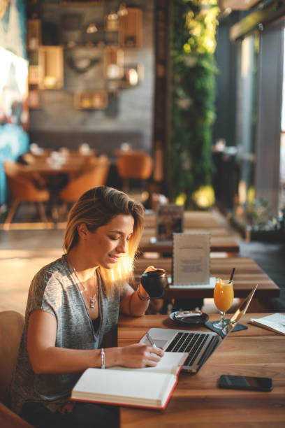 istock Young woman writing a note with pen with laptop on table at a coffee shop. 1189557917