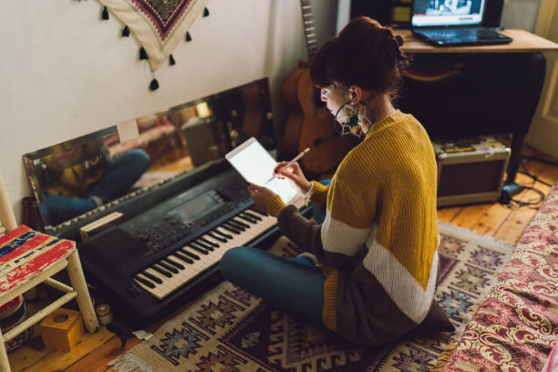 Young woman composing new music at home Hippie woman sitting on floor and using tablet to create new music woman sitting on piano stock pictures, royalty-free photos & images