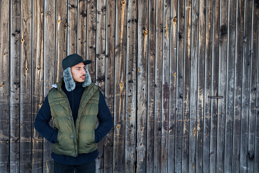 Front view portrait of young man standing against wooden background outdoors in winter. Copy space.