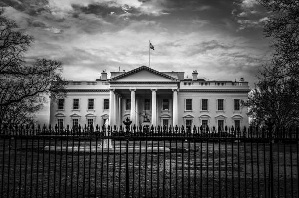 View of the front entrance to the White House in Washington DC with iron fence in the foreground Black and white image of the United States presidential residence with flag on roof in the nations capital ominous photos stock pictures, royalty-free photos & images