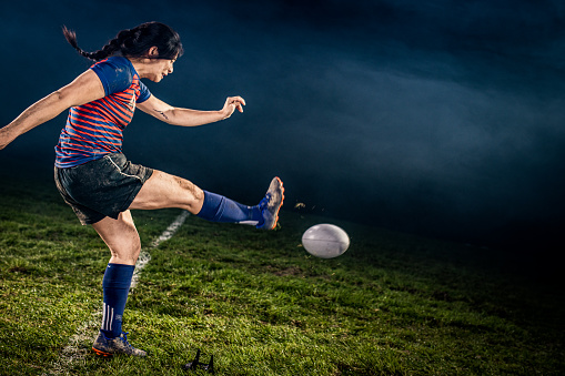 Female rugby player kicking ball on field.