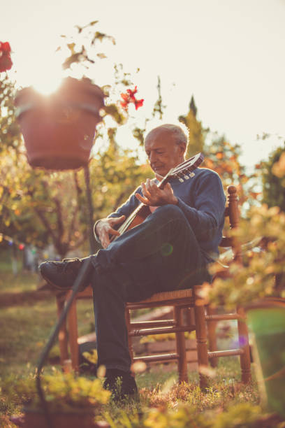 homme aîné jouant sur un instrument à cordes dans son jardin - autumn table setting flower photos et images de collection