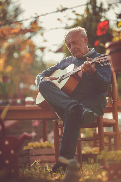 homme aîné s'asseyant et jouant une guitare - autumn table setting flower photos et images de collection