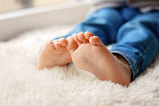Cozy holidays at home. Close up photo of little child barefooted feet sitting on white furry blanket at window. Winter season lifestyle. Leisure time. Sweet childhood. Copy space stock photo