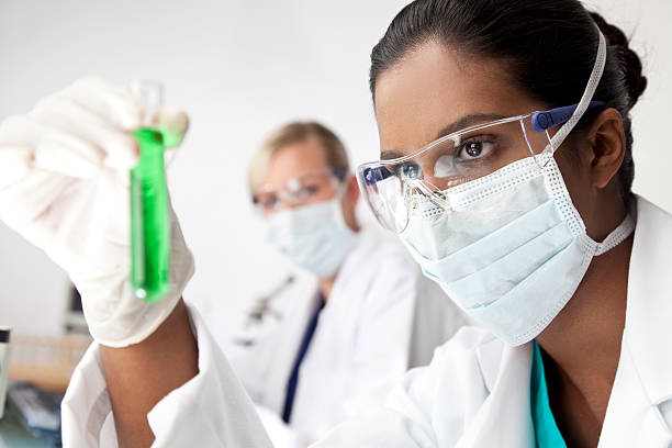 Asian female scientist examines test tube of green solution stock photo