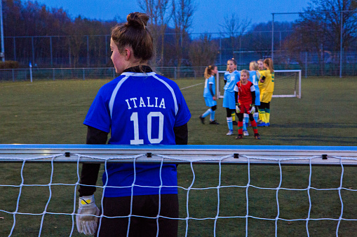 The young female goalkeeper competing for the ball during a football match on a dark autumn evening
