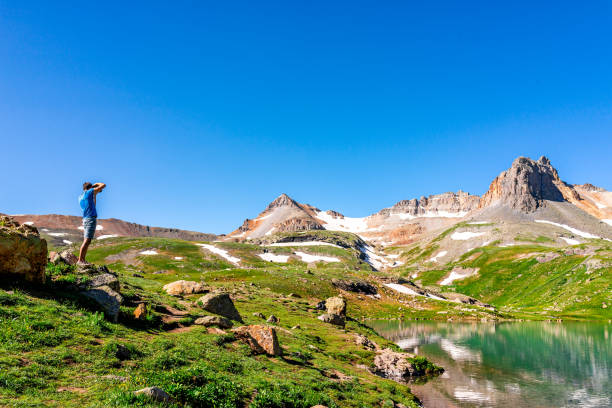 Landscape view of green meadow and Ice lake water near Silverton, Colorado in August 2019 summer and man taking picture on summit Landscape view of green meadow and Ice lake water near Silverton, Colorado in August 2019 summer and man taking picture on summit ice lakes colorado stock pictures, royalty-free photos & images