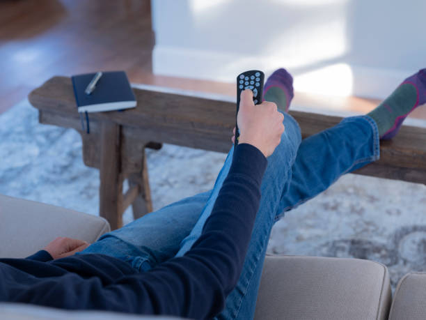 istock Person sitting on couch holding TV remote control 1189609461