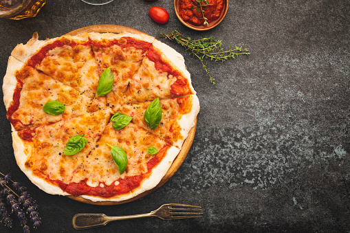 Tasty margharita pizza and cooking ingredients on black concrete background. Flat lay with space.