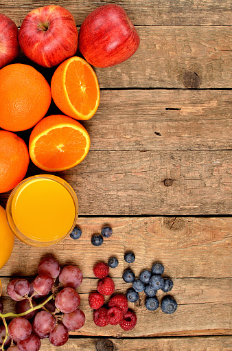 Orange juice, fresh oranges, apples, grapes, raspberries and blueberries on a wooden table - view from above - vertical photo - left orientation frame