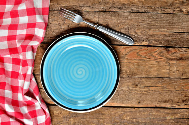 istock Blue ceramic plate, fork and red checkered tablecloth left frame on old vintage wooden table background - view from above 1189616467