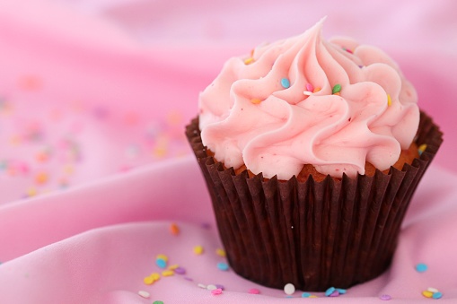 Pink cupcake with buttercream frosting on a pink tablecloth