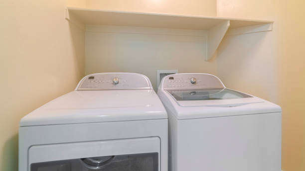 istock Panorama frame Washing machine and dryer inside a laundry room with shelf and beige wall 1189642889