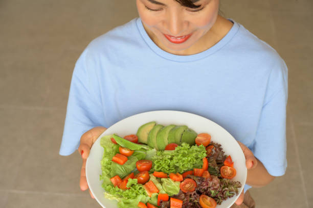 Healthy asian woman happy smiling with mixed salad plate in hand from top view on floor background.