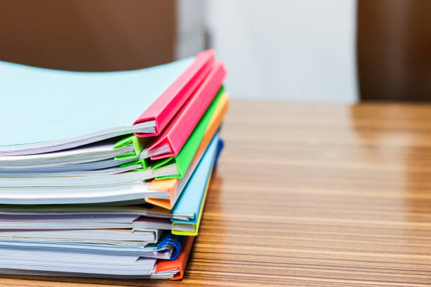 istock Pile of unfinished paperwork stacked in archive with plastic slide binder bars on office table waiting to be managed and inspected for score. Report papers stacks. Business and education concept. 1189678821