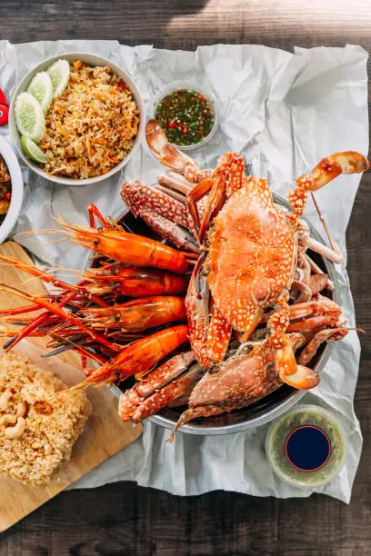 Top view of steamed Flower Crabs and Grilled Prawns (Shrimps) with Crab Cracker on paper with other seafoods in background.