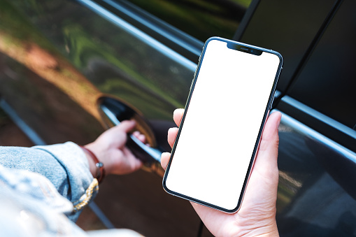 Mockup image of a woman holding and using mobile phone with blank screen while opening the car door