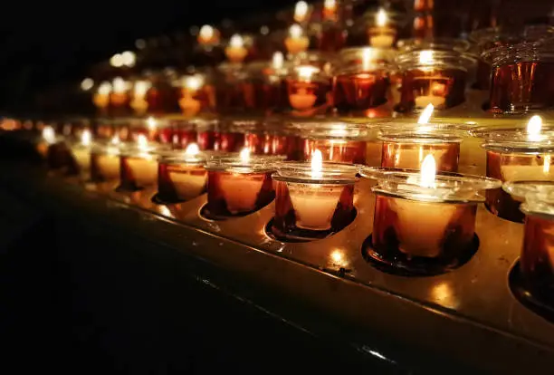 Photo of Candles in a church, cathedral or temple, in yellow transparent candlesticks. The concept of mourning. We remember, we grieve. Selective focus, side view, copy space