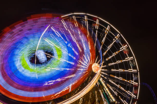 due giostre in movimento nel parco divertimenti, illuminazione notturna. lunga esposizione. - ferris wheel wheel night neon light foto e immagini stock