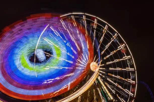 Photo of Two rides in motion in amusement park, night illumination. Long exposure.