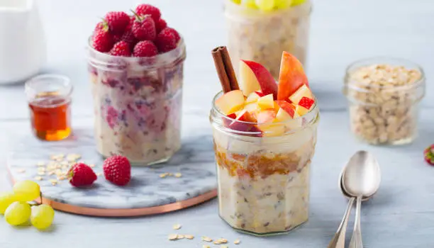 Overnight oats, bircher muesli with raspberry, apple in glass jars on wooden background. Close up.