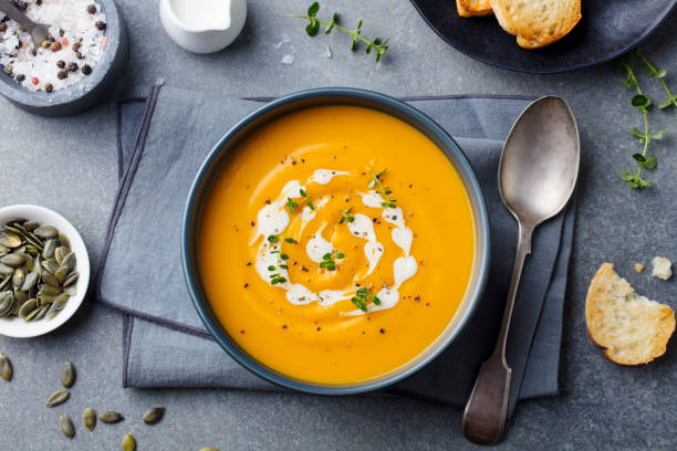 Pumpkin and carrot soup with cream on grey stone background. Top view. Pumpkin and carrot soup with cream on grey stone background. Top view. soup lentil healthy eating dishware stock pictures, royalty-free photos & images