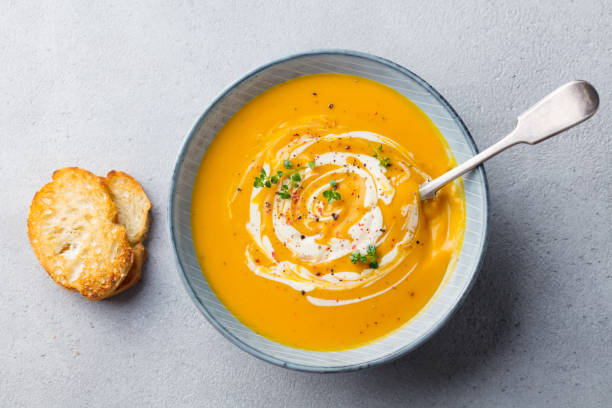 Pumpkin and carrot soup with cream on grey stone background. Top view.