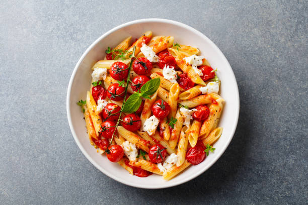 Pasta penne with roasted tomato, sauce, mozzarella cheese. Grey stone background. Top view. Pasta penne with roasted tomato, sauce, mozzarella cheese. Grey stone background. Top view. looking down stock pictures, royalty-free photos & images