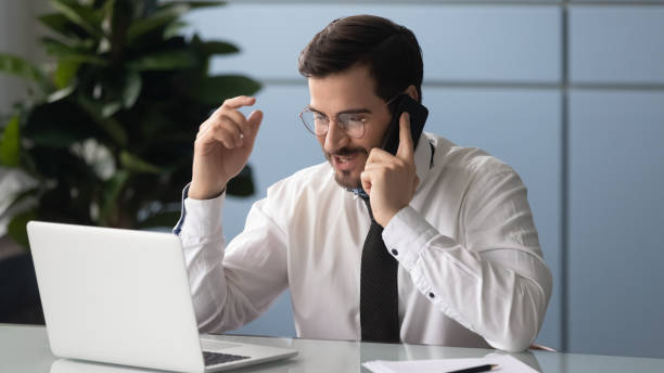 istock Young businessman talk on cell using laptop in office 1189709693