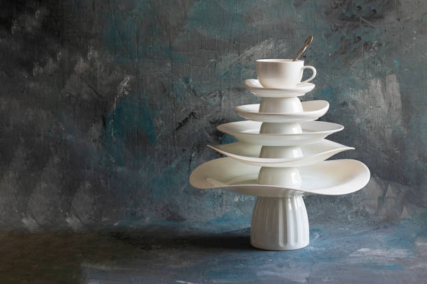 Pyramid made from white dishes, Christmas tree shape with tea couple on top on dark background. Creative concept about dishware, kitchen, restaurant, postcard, Xmas, New Year. Horizontal, copy space