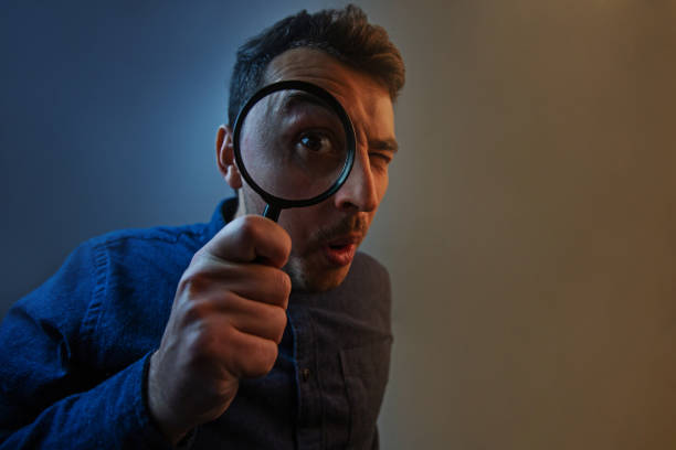 灰色の背景に虫眼鏡を持つショックを受けた男。灰色の背景に隔離された虫眼鏡を持つ好奇心旺盛な若者。 - magnifying glass lens holding europe ストックフォトと画像