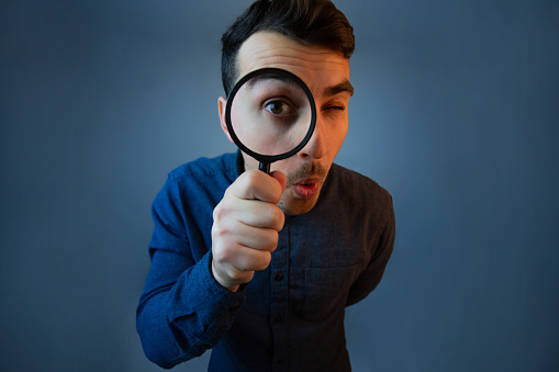 Curious young man with magnifying glass Isolated on grey background. Surprised Young man student holding magnifying glass.