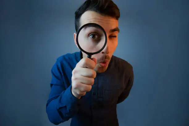 Photo of Curious young man with magnifying glass Isolated on grey background.