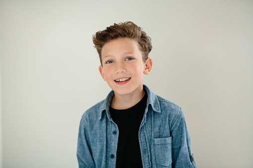 Studio portrait of a smiling little boy wearing casual clothing standing alone against a gray background
