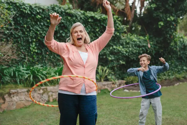 Laughing Grandmother playing with a hula hoop with her cute little grandson in her backyard at home