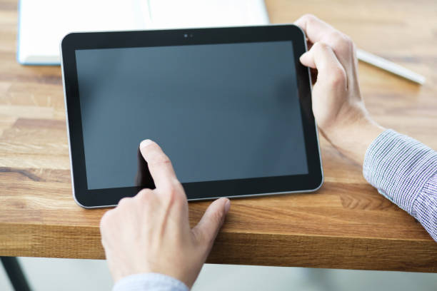 istock Man's hands holding blank tablet device over a wooden work-space table. 1189739556