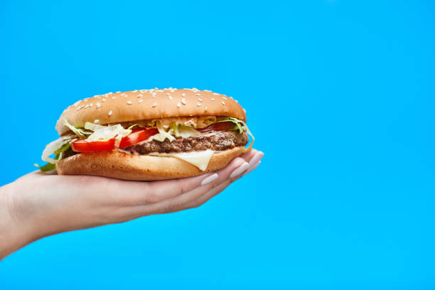 istock Woman Hands holding a hamburger on a blue background 1189741203